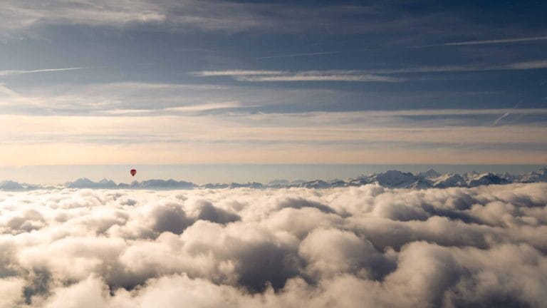 Vue d’une montgolfière survolant une mer de nuages, avec les Alpes en arrière-plan