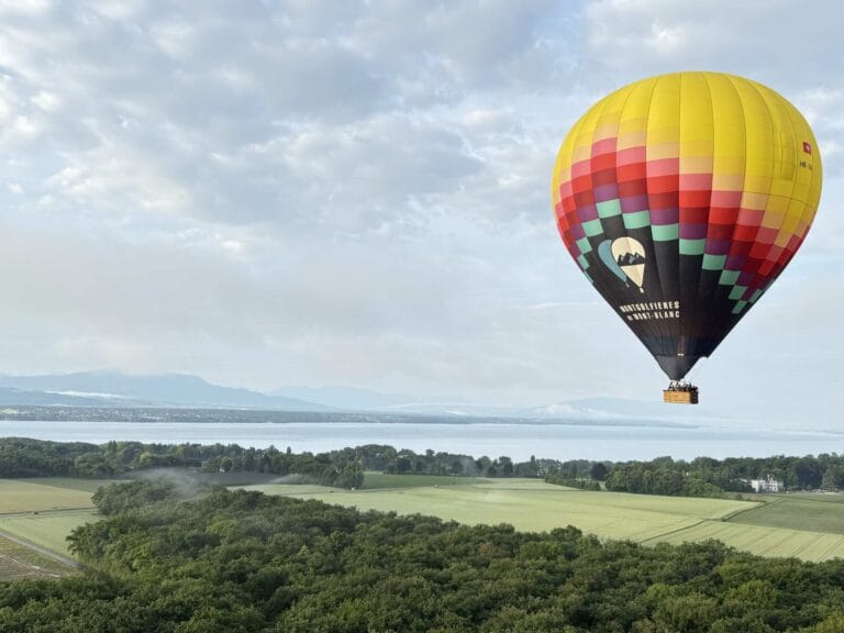 Montgolfière flottant au-dessus d’un champ verdoyant, avec le lac Léman au loin